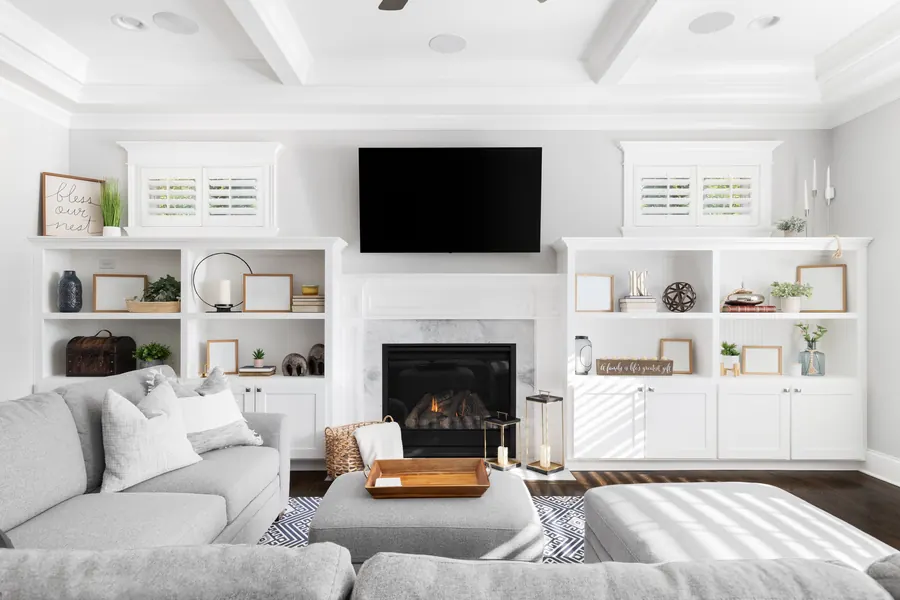 White living room with a TV mounted above the fireplace between built-in shelves