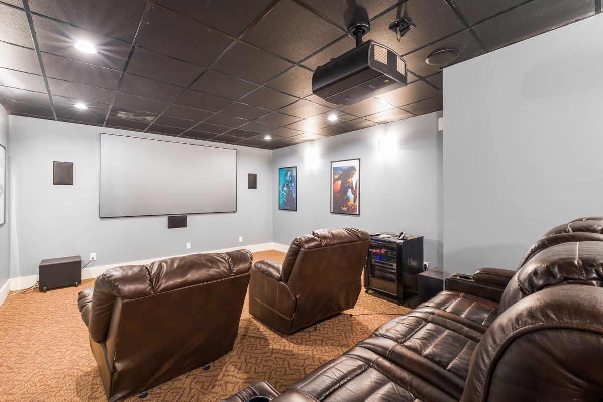 A modern home theater room with comfortable seating, a large screen, and elegant wood paneling and black acoustic walls